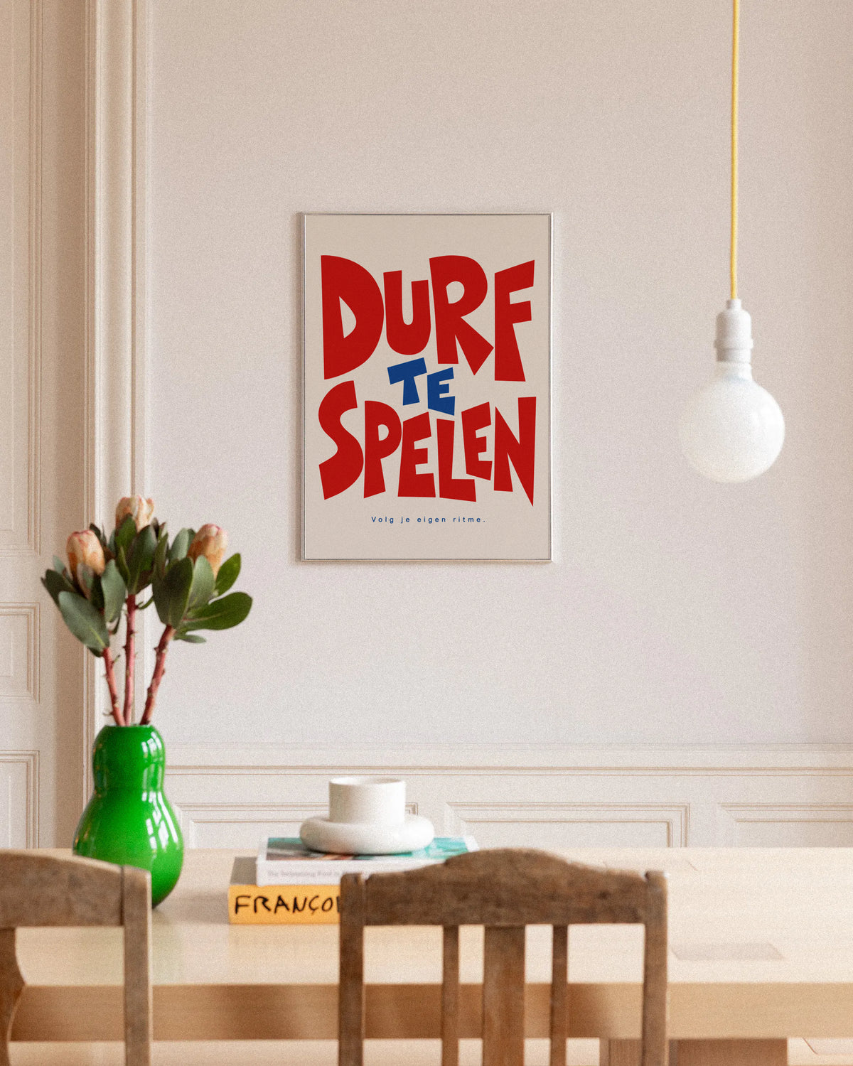 Poster in een interieur: Grafische tekst DURF TE SPELEN in rood en blauw met Volg je eigen ritme op een lichte achtergrond