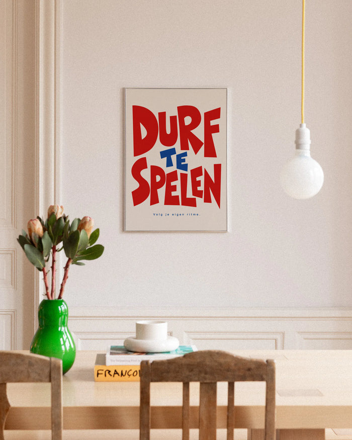 Poster in een interieur: Grafische tekst DURF TE SPELEN in rood en blauw met Volg je eigen ritme op een lichte achtergrond