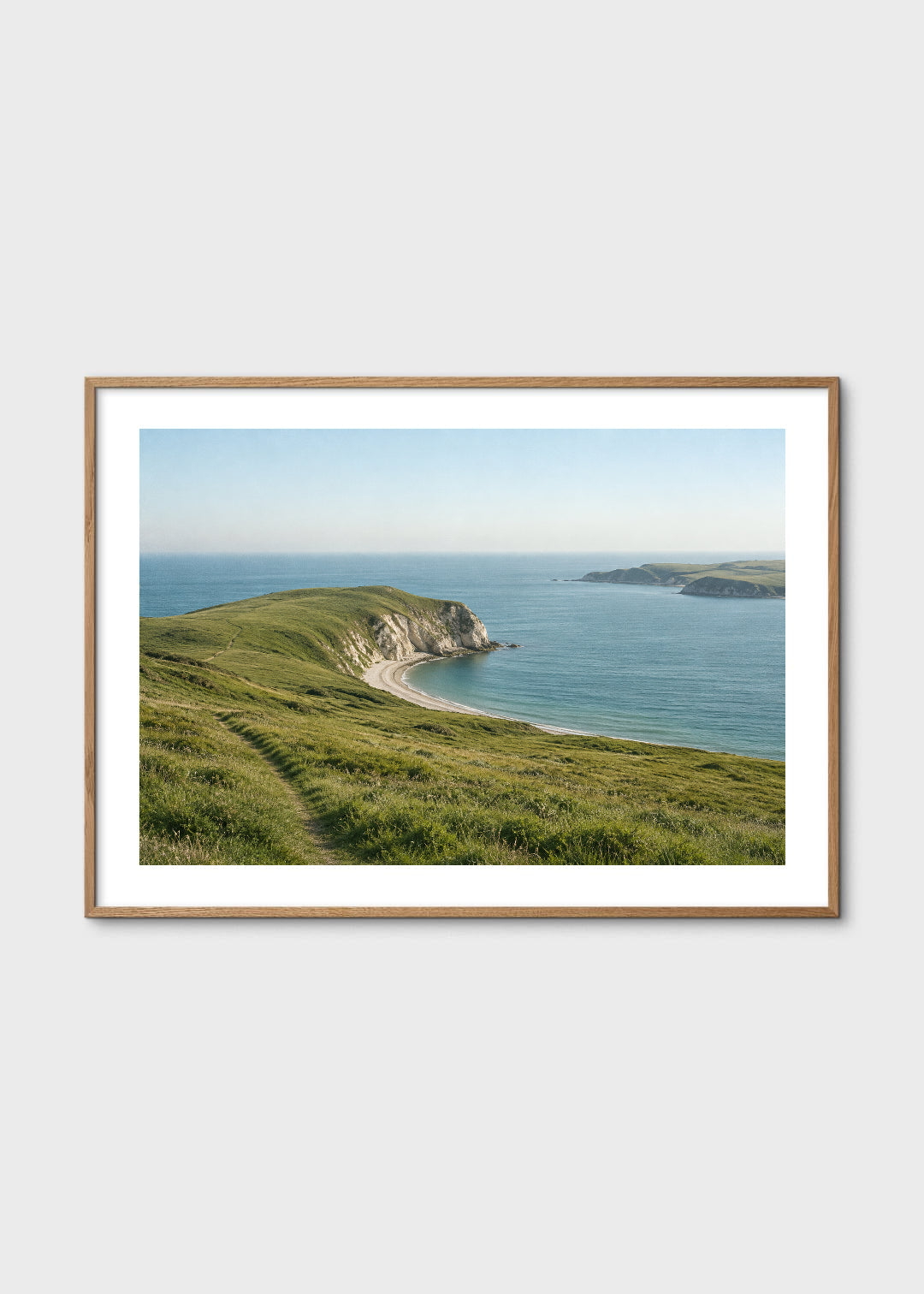 Ingelijste poster: Panorama van een groene kaap met een wandelpad, lichte kliffen en een beschutte blauwe baai