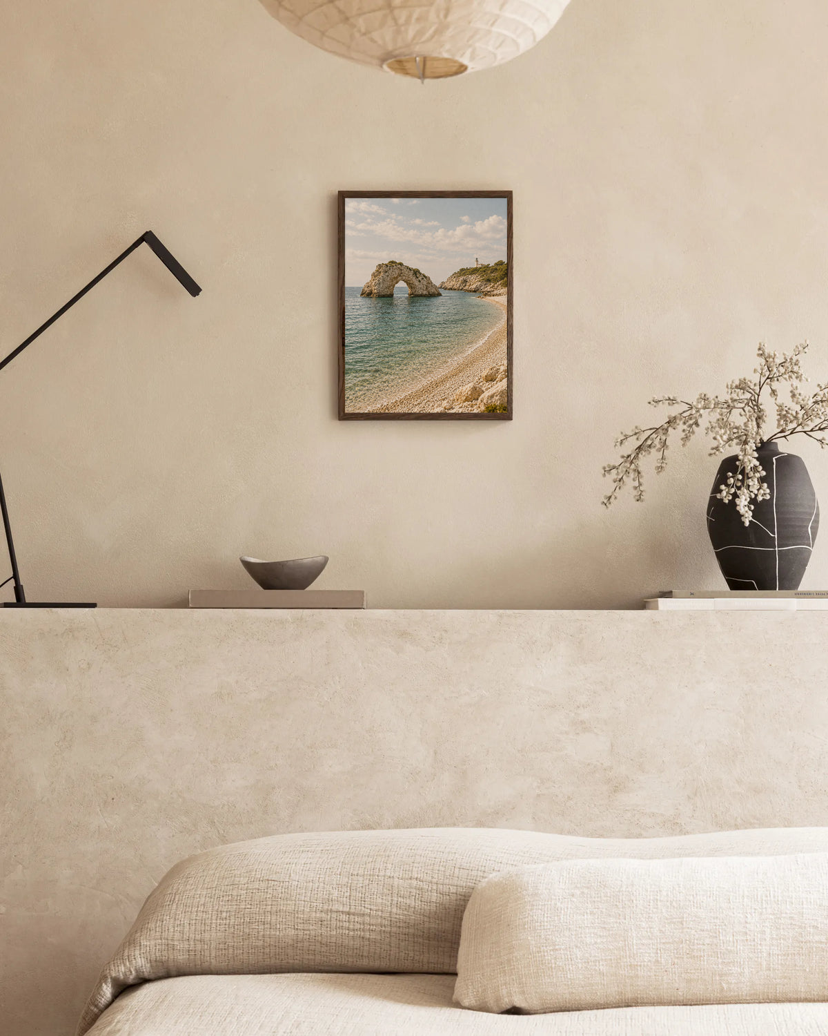 Poster in een interieur: Natuurlijke rotsboog in helder zeewater naast een kiezelstrand en een kleine vuurtoren