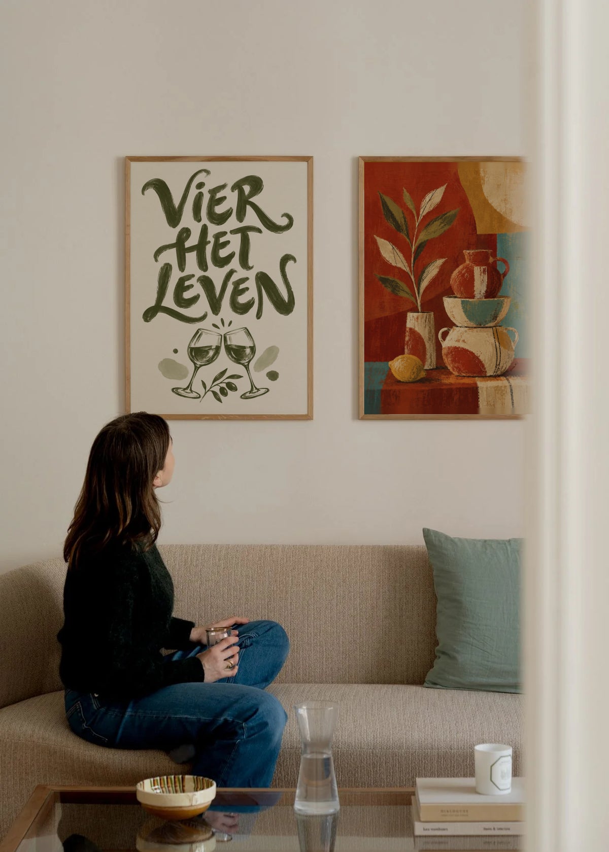 Poster in een interieur: Olijfgroene tekst VIER HET LEVEN boven twee klinkende wijnglazen en bladeren op crème