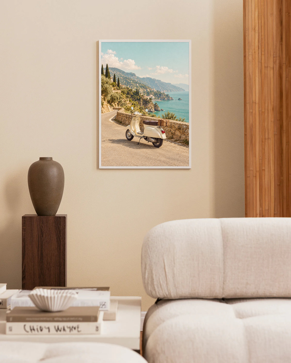 Poster in een interieur: Crèmekleurige scooter met rieten mand langs een stenen muur met uitzicht op een zonnige kust